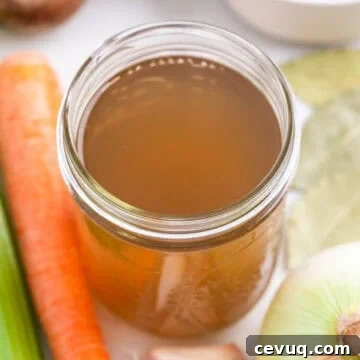 Homemade vegetable broth in a glass jar with vegetables around it