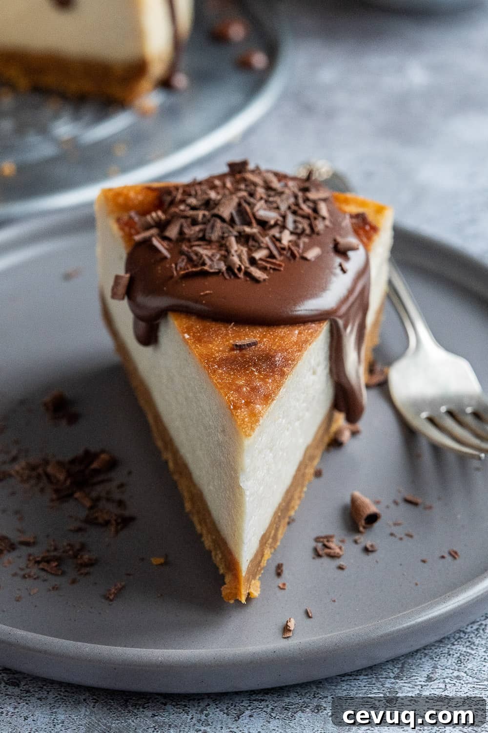Close up of a slice of cheesecake topped with ganache on a grey plate.