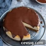 Cheesecake topped with chocolate ganache on a metal plate on a grey background with a bowl of ganache and three forks.