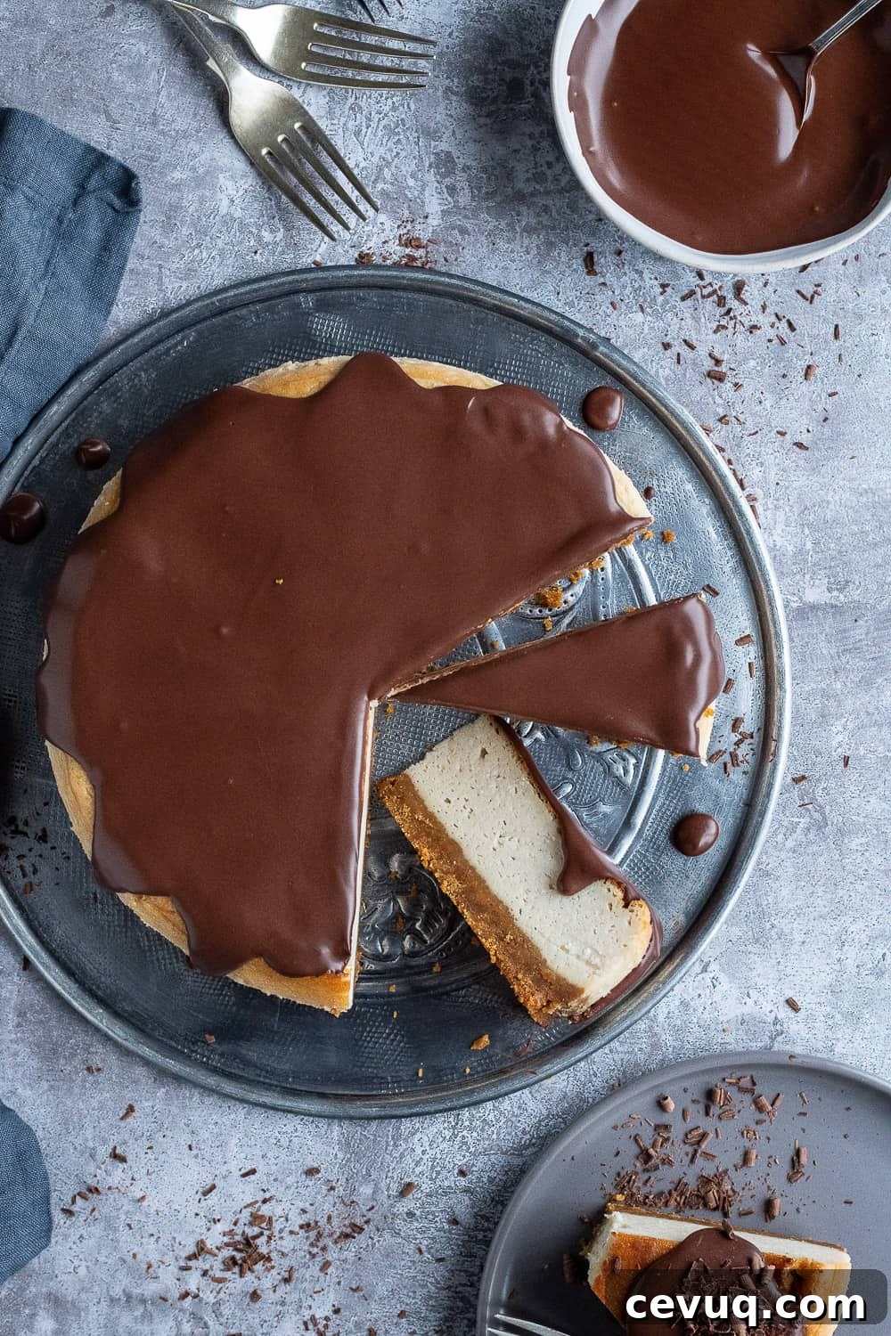 Top down shot of vegan Baileys cheesecake cut into slices on a metal plate with one slice on a grey plate and a bowl of chocolate ganache.