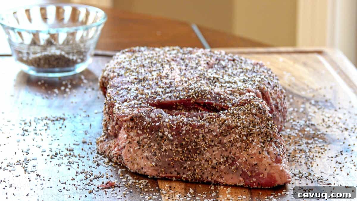 Beef chuck roast covered in salt and pepper on cutting board with seasoning dish