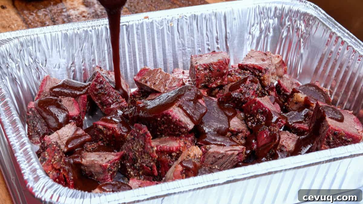 Barbecue sauce being poured over smoked chuck roast in aluminum pan