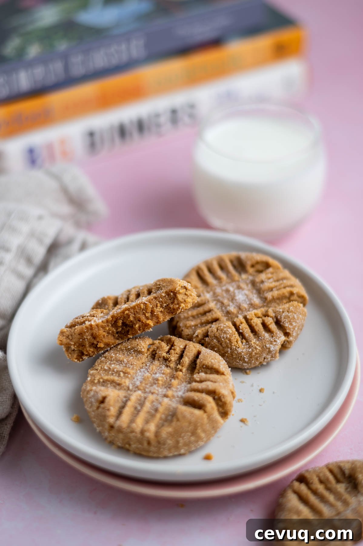 three peanut butter cookies on a plate with a glass of milk and cookbooks in the background