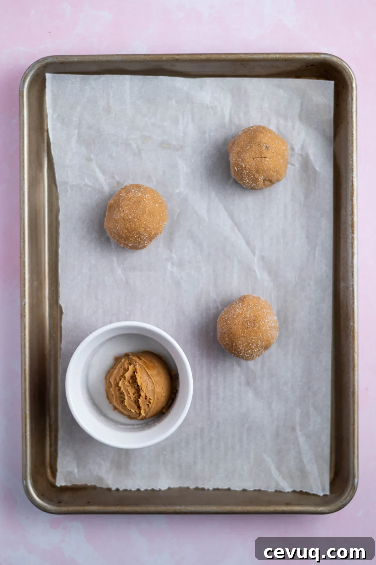cookie dough balls on a parchment lined baking sheet; one cookie in a small bowl of granulated sugar