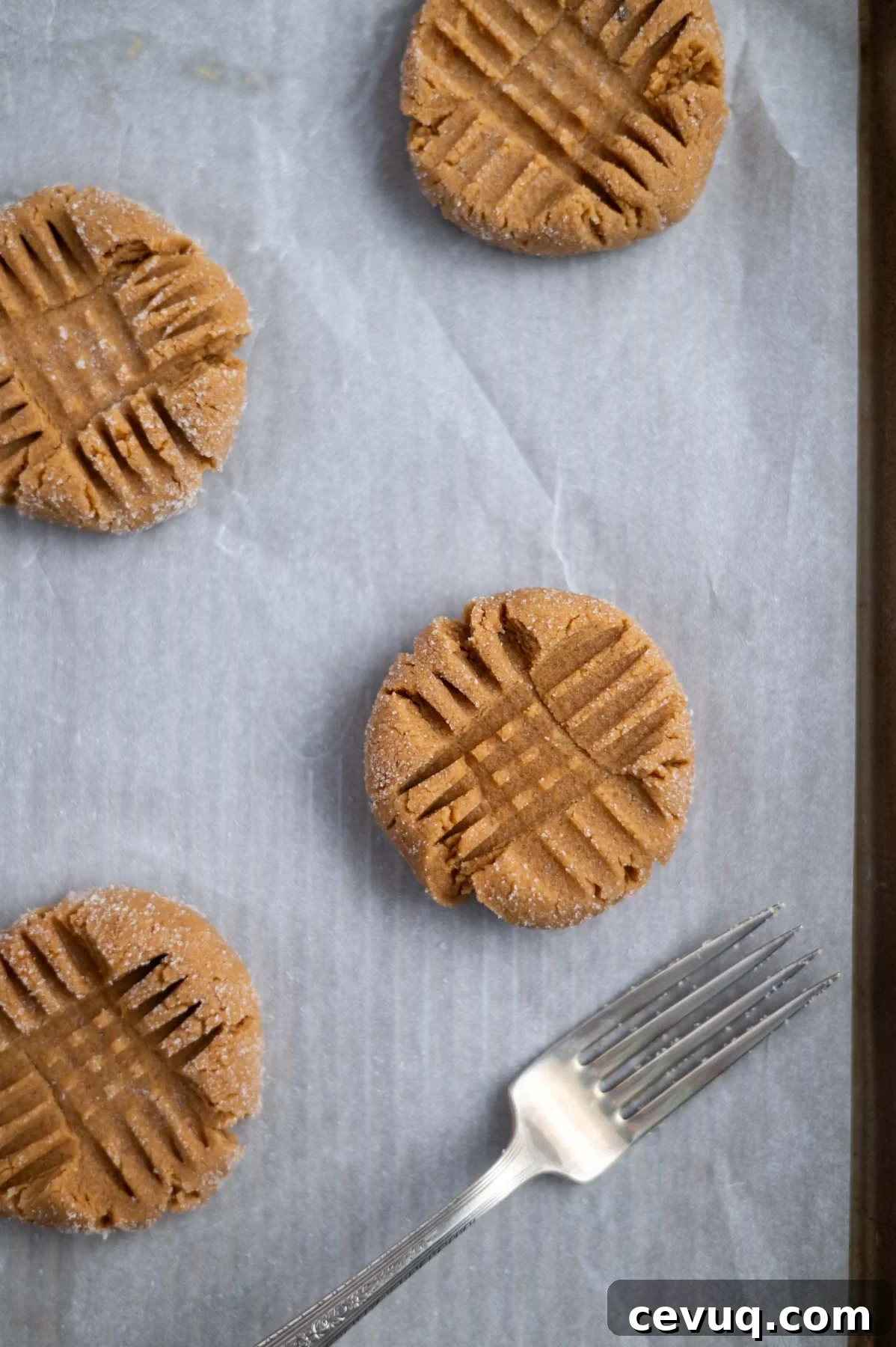 peanut butter cookies on a parchment lined baking sheet with crisscross marks