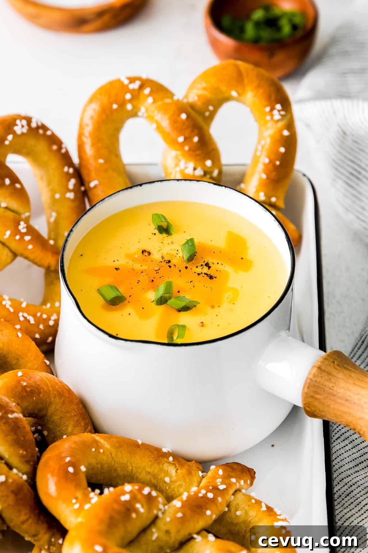 A saucepan full of beer cheese dip surrounded by soft pretzels.