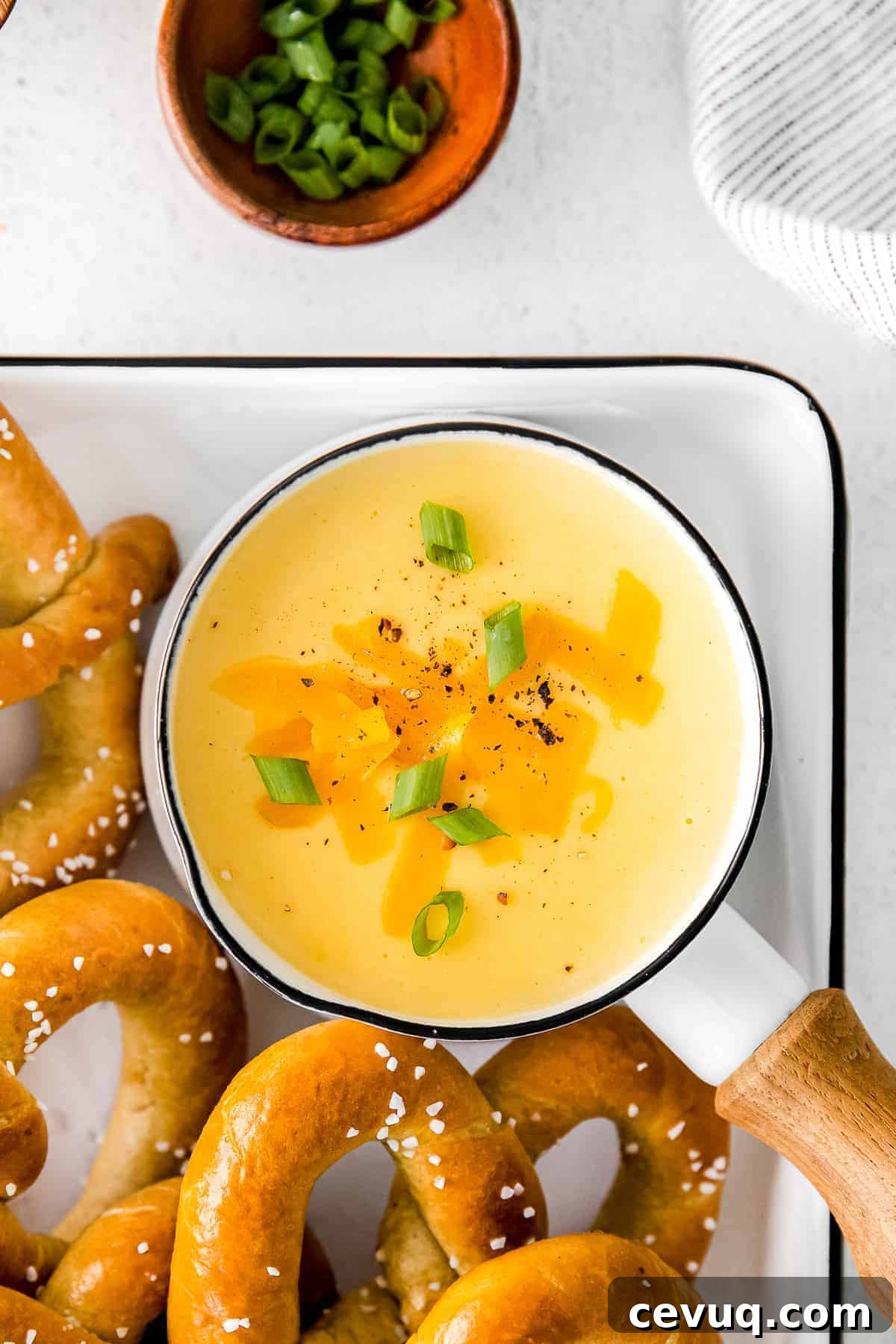A saucepan of beer cheese dip topped with chopped green onions.
