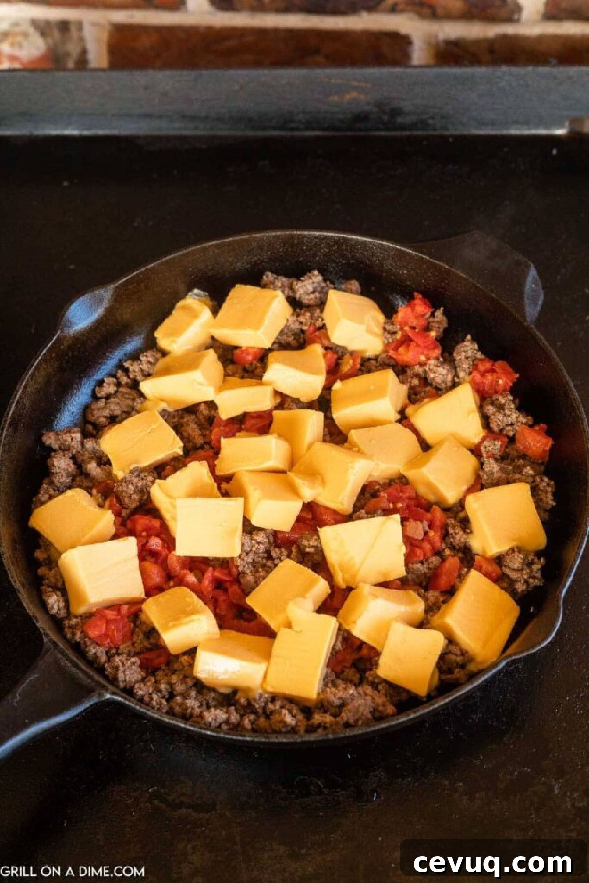 Top diced velveeta cheese and Rotel on the ground beef in a cast iron skillet on the griddle
