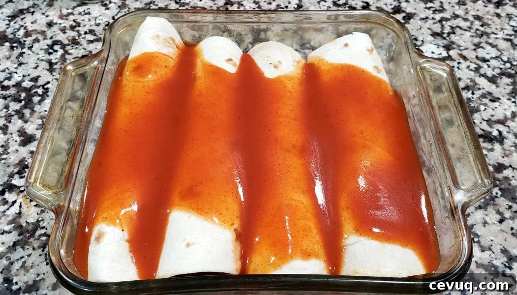 four chicken enchiladas rolled up in a baking dish topped with enchilada sauce