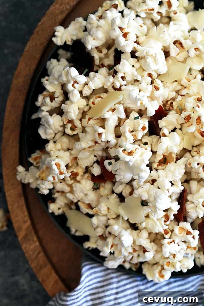 A bowl of Rosemary Parmesan Bacon Popcorn garnished with rosemary and shaved Parmesan.