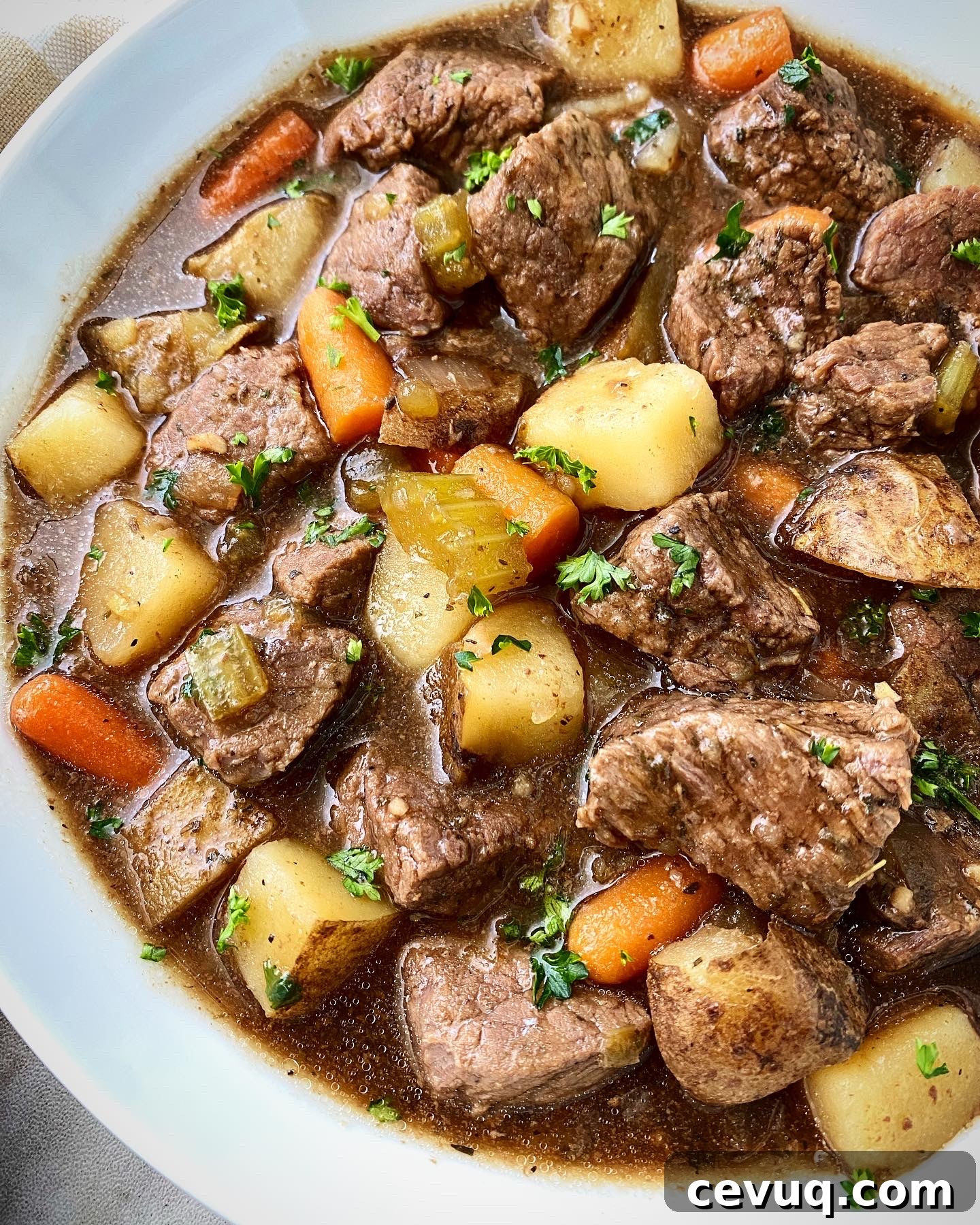 close up shot of cooked Guinness beef stew in a white bowl with a silver spoon