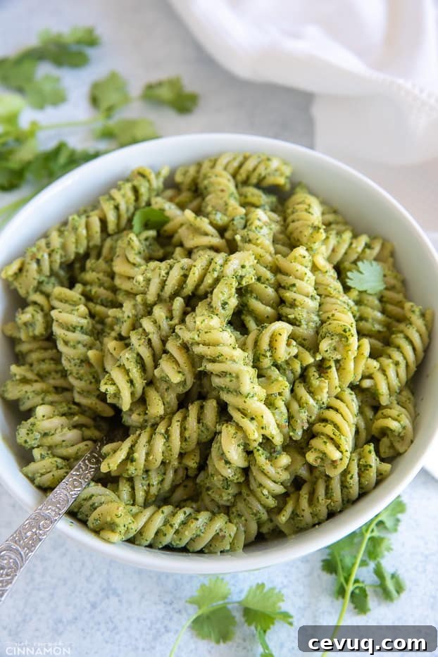 closeup of a bowl of creamy cilantro pasta tossed with rotini pasta with a fork and fresh cilantro