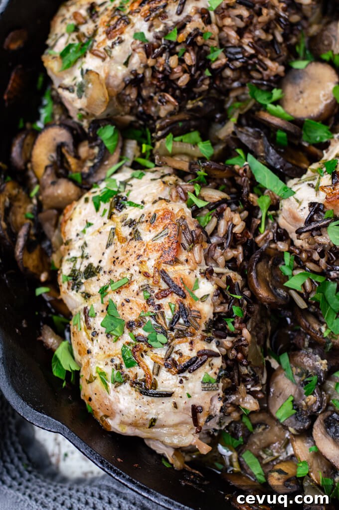 A wild rice stuffed pork chop sits on top of sautéed mushrooms. Chopped parsley is sprinkled on top.