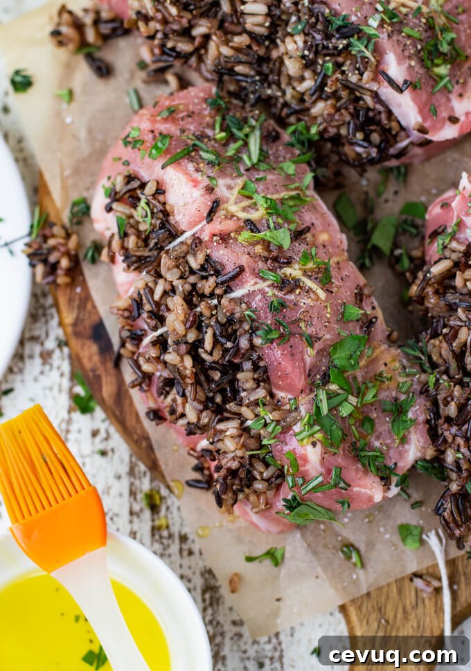 A pork loin chop stuffed with wild rice and tied with kitchen twine and sprinkled with fresh herbs. A pastry brush sits on the edge of a bowl with olive oil.