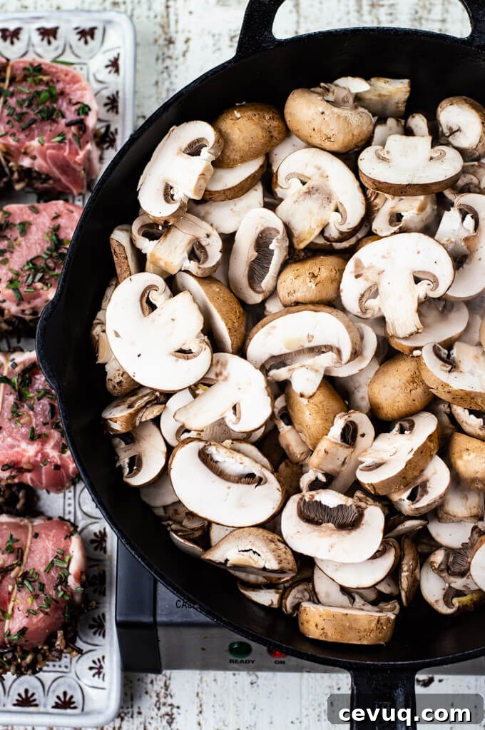 A cast iron skillet with raw sliced mushrooms. Four wild rice stuffed pork chops sit on a platter next to it. 