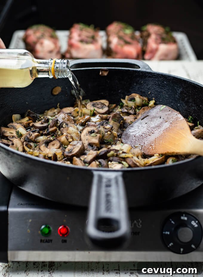 A cast iron skillet of satuéed mushrooms and onions with a bottle of white wine being poured in. Four stuffed pork chops are blurred in the background.