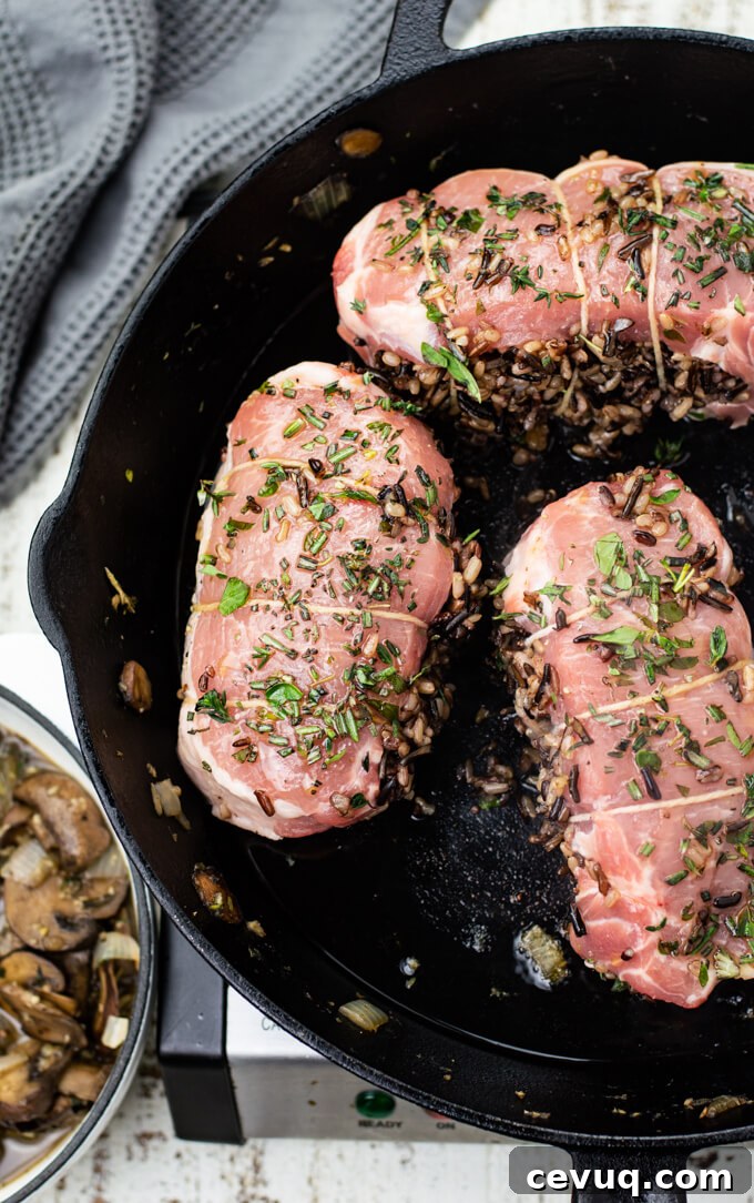Three wild rice stuffed pork chops are cooking in a cast iron skillet. 