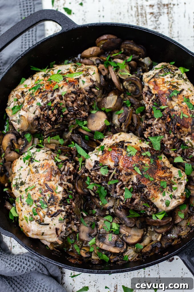 A cast iron skill with mushrooms and wild rice stuffed pork chops sitting on top of the mushrooms. Chopped parsley is sprinkled on top.