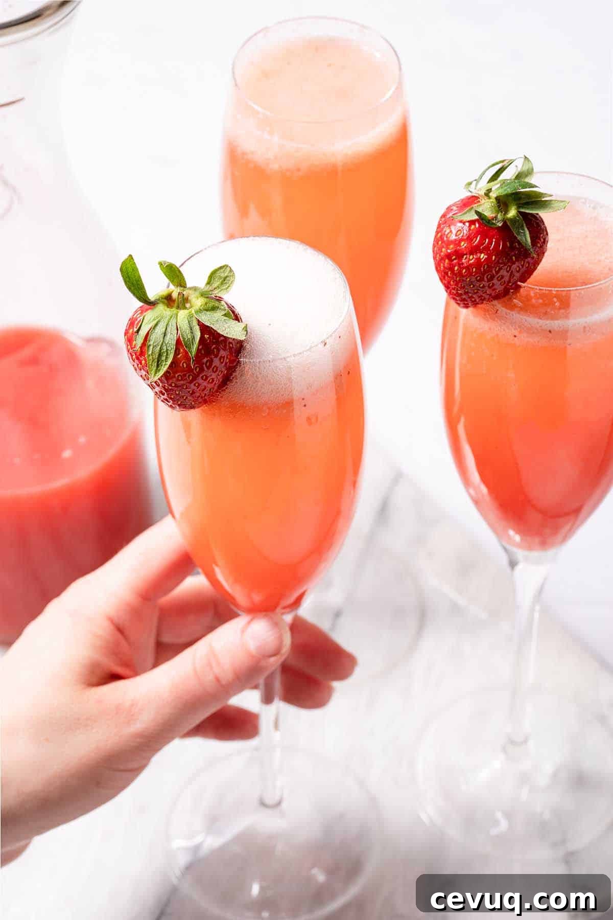 hand holding strawberry mimosa with two other mimosas on the side