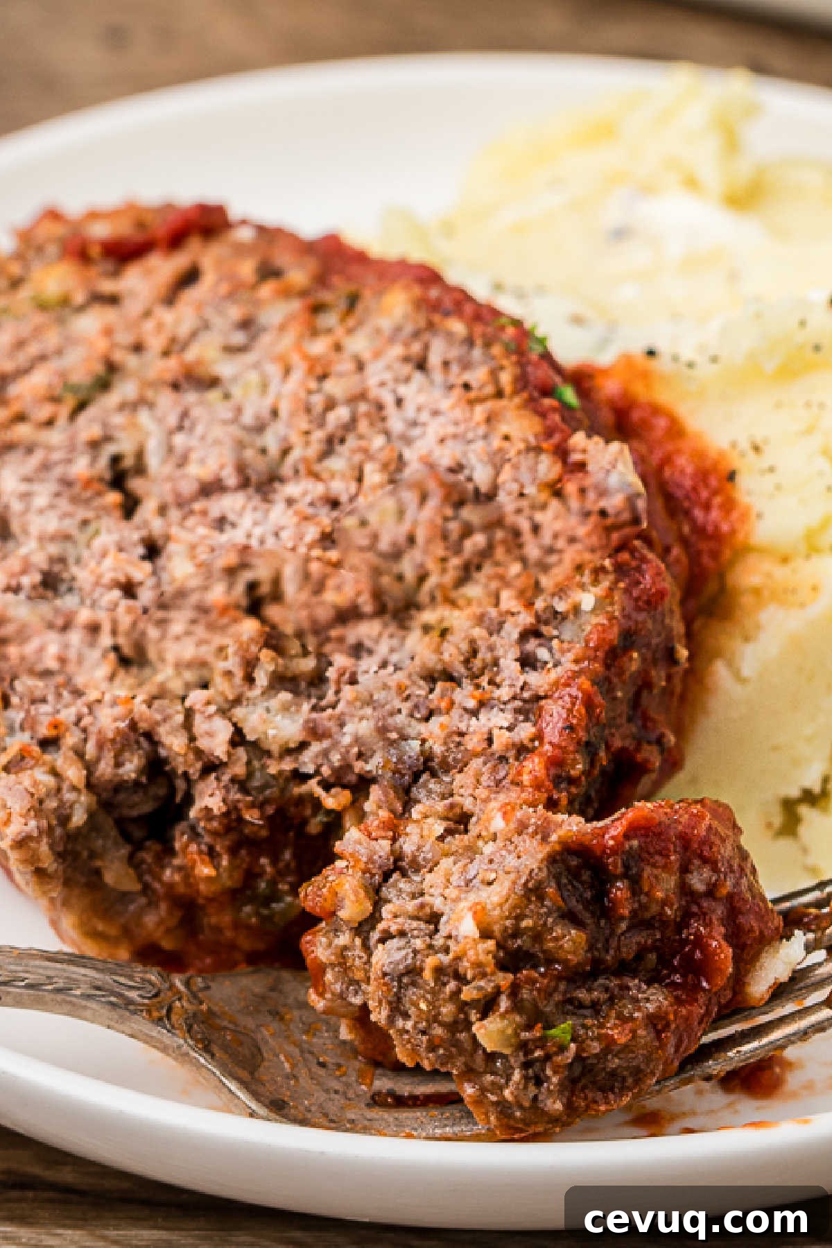 Close up view of a slice of Cajun meatloaf with mashed potatoes.