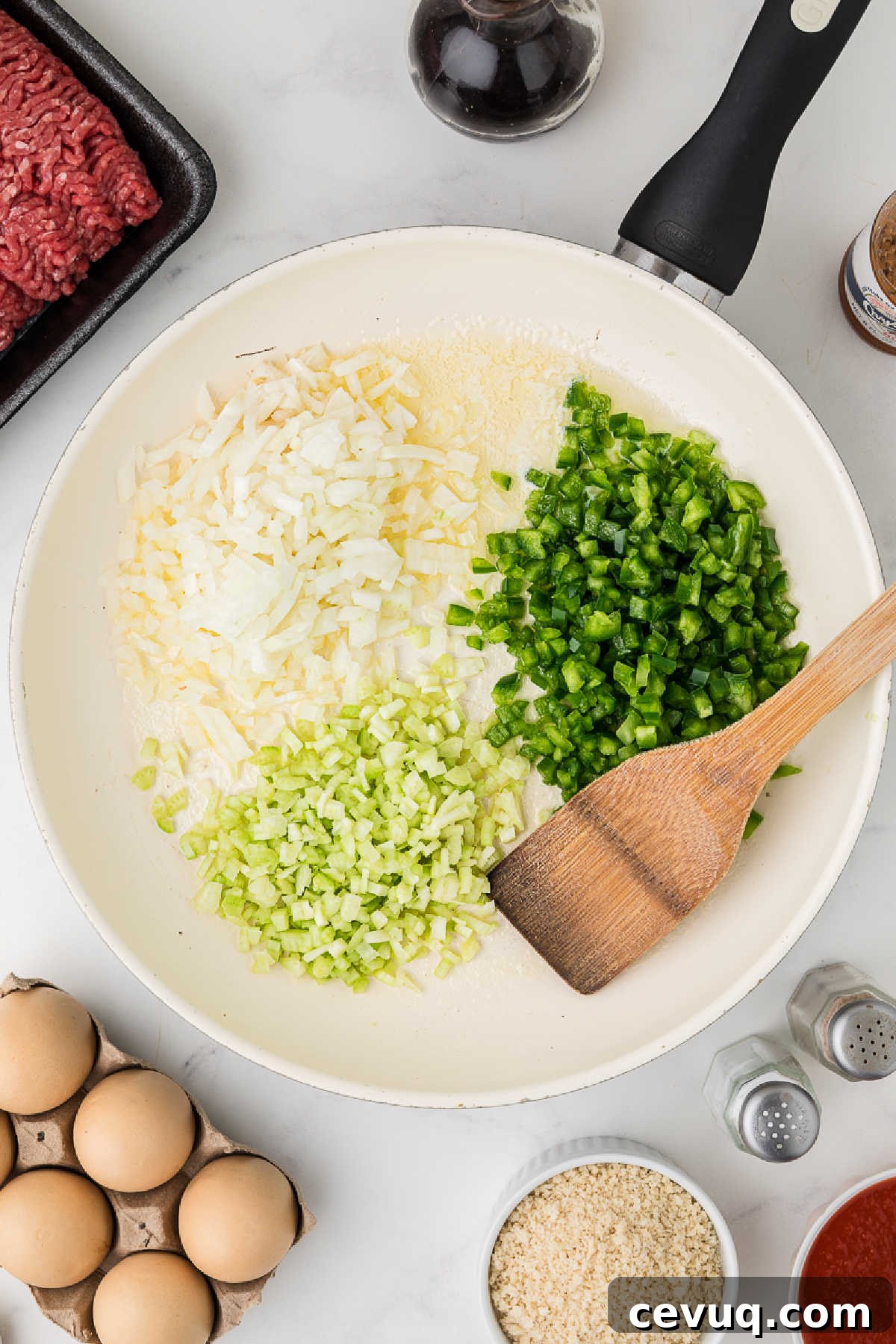 A large skillet with onions, bell peppers and celery.