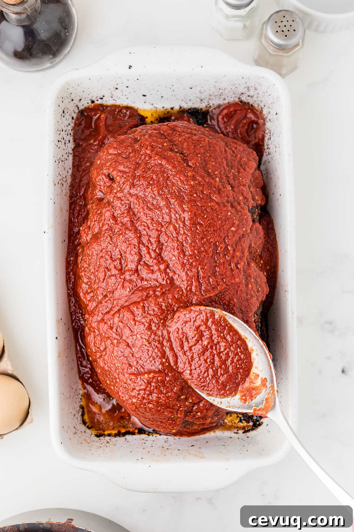 Tomato sauce being spread on top of a Cajun meatloaf.