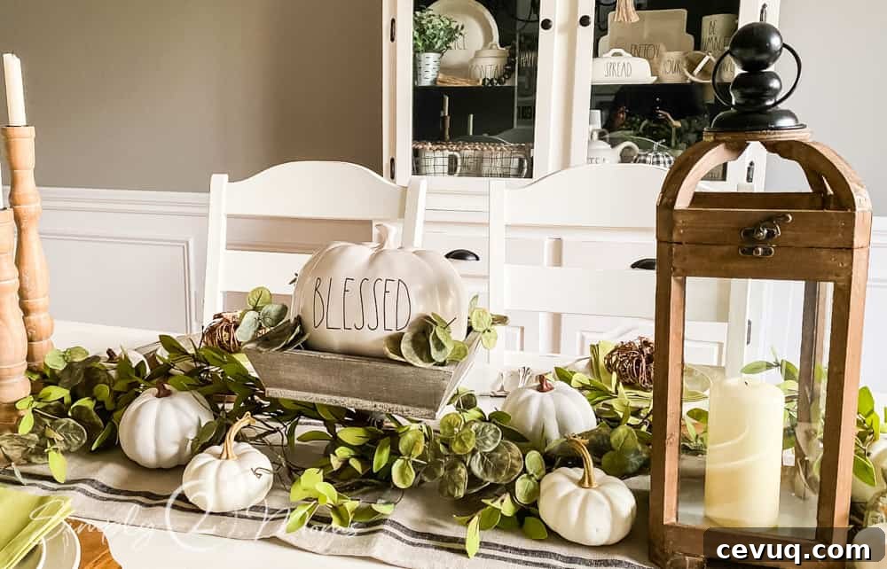 close up of rae dunn pumpkin in wood pedastal bowl with greenery and mini pumpkins on table