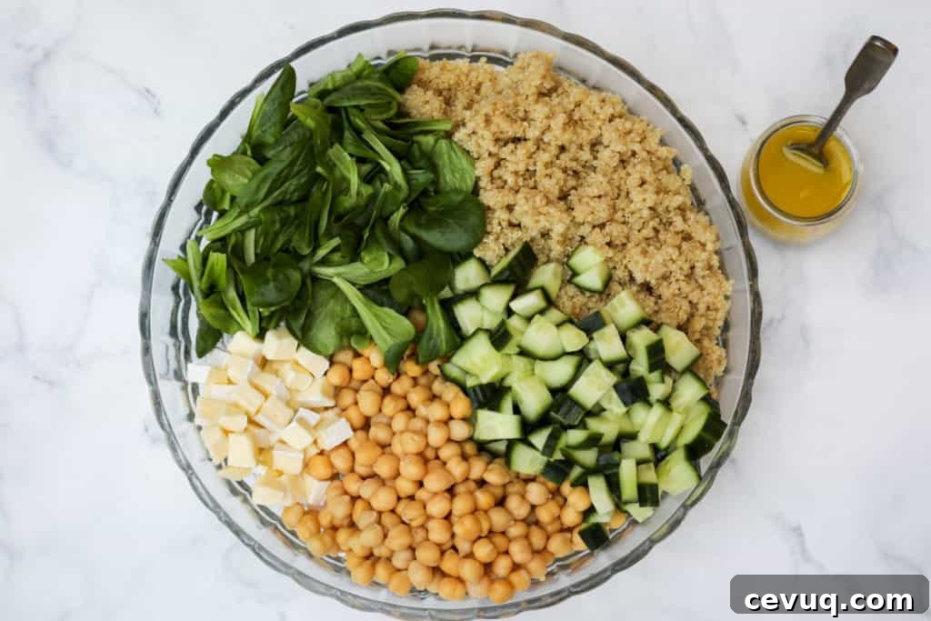 Glass bowl of quinoa chickpea salad with quinoa, cucumber, chickpeas, mache, and brie