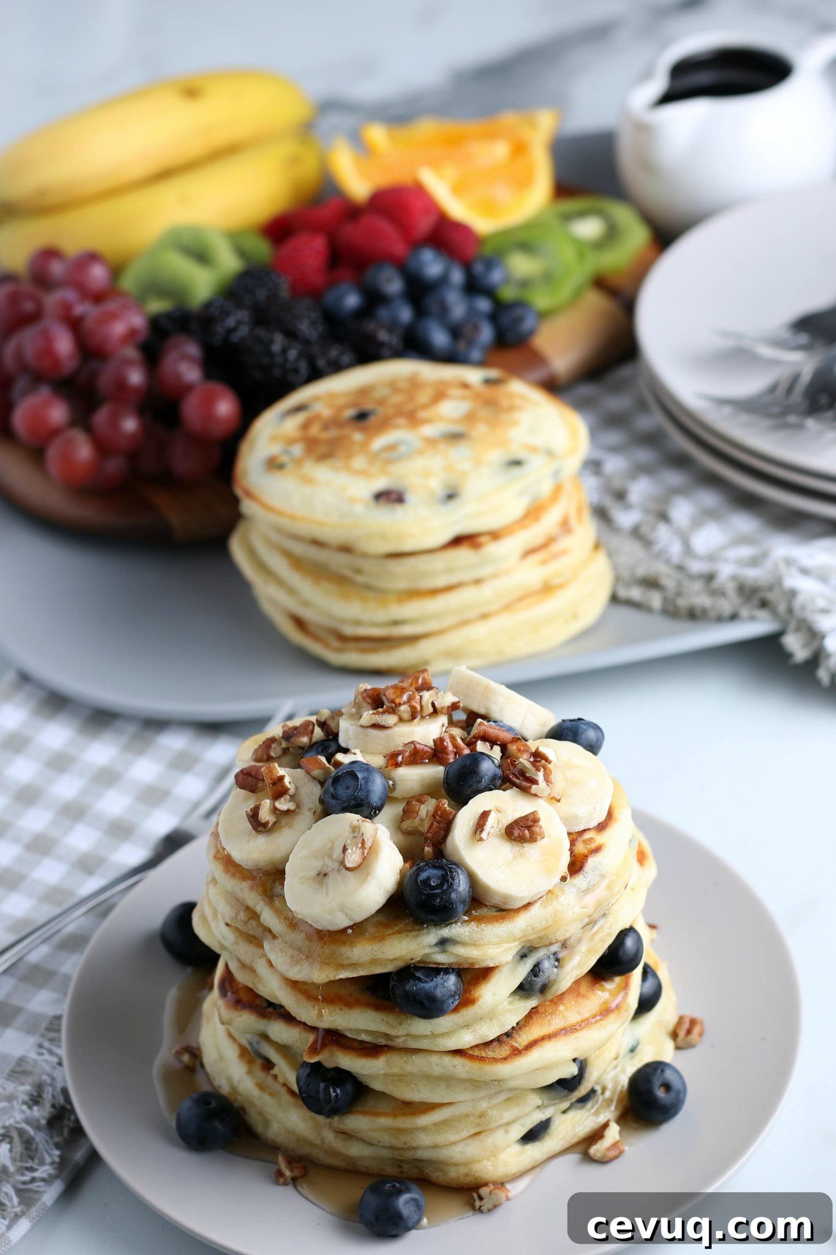 A stack of blueberry pancakes with fruit in the background.
