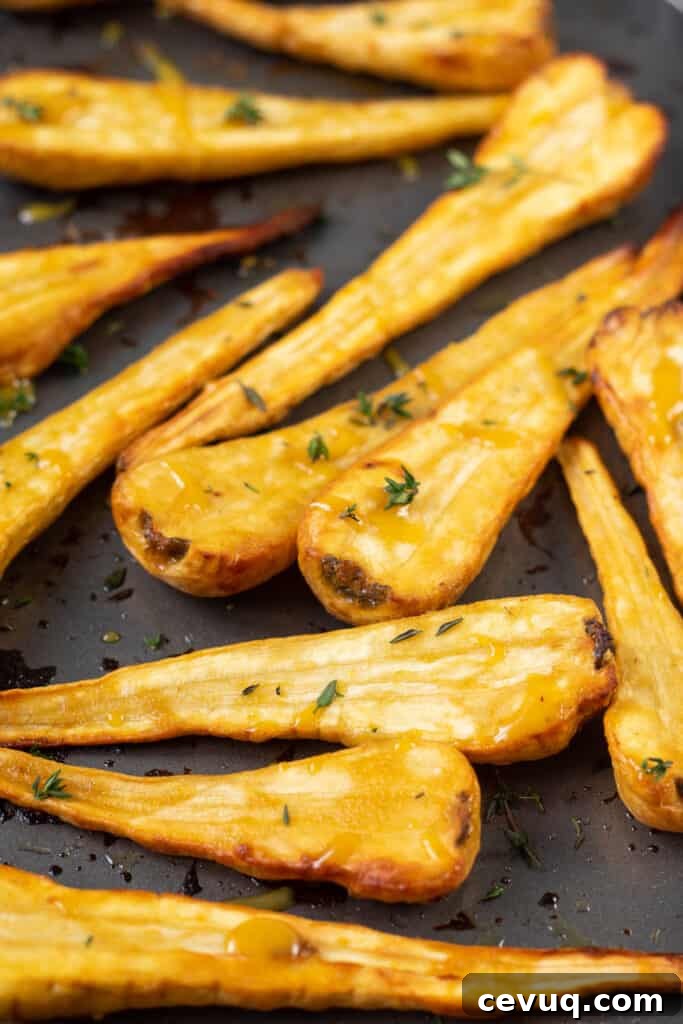 Crispy Roasted Parsnips with Honey and Thyme 7 mustard and maple glazed parsnips close up front facing on baking tray with chopped thyme.