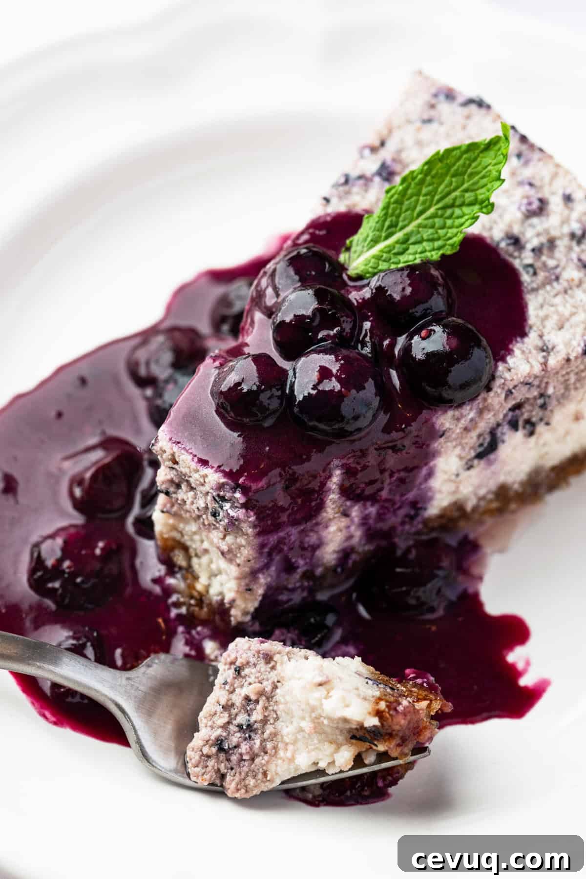 A slice of vegan blueberry cheesecake topped with blueberry sauce with a piece out of it.