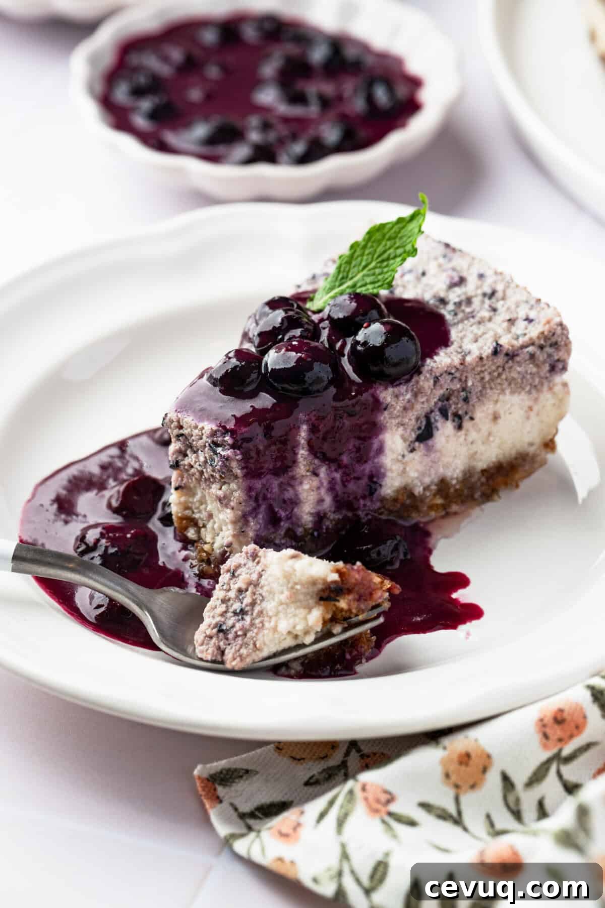 A piece of blueberry cheesecake on a plate with blueberries on top of it wth a bite taken out of it.