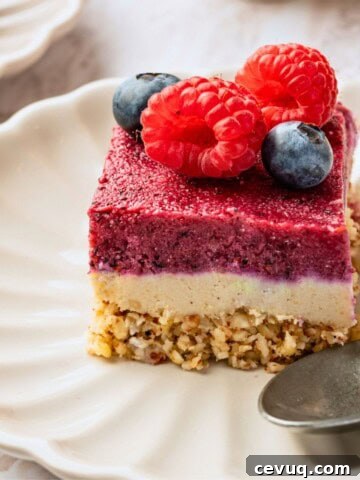 A dessert bar with a crumble layer, white layer and pink layer on a plate.