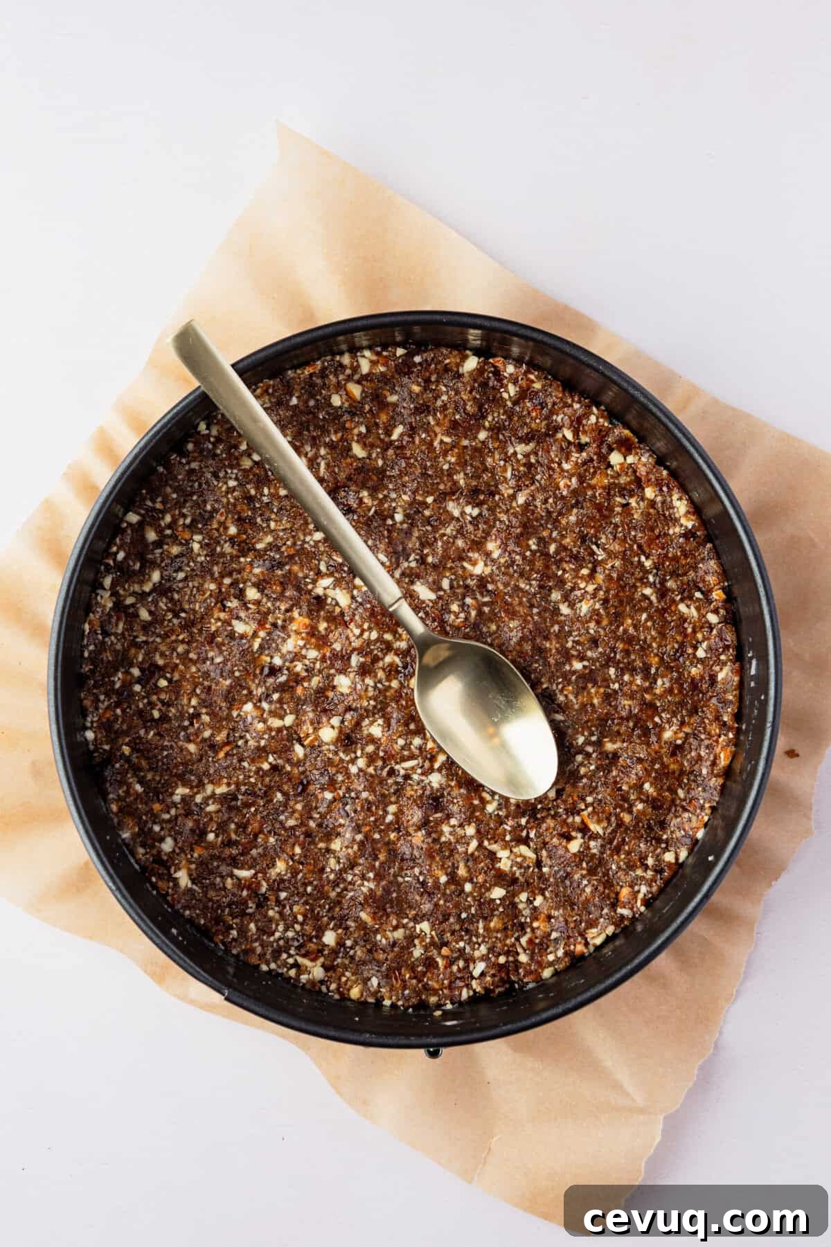 A springform pan with a crust in it with a spoon on the crust.