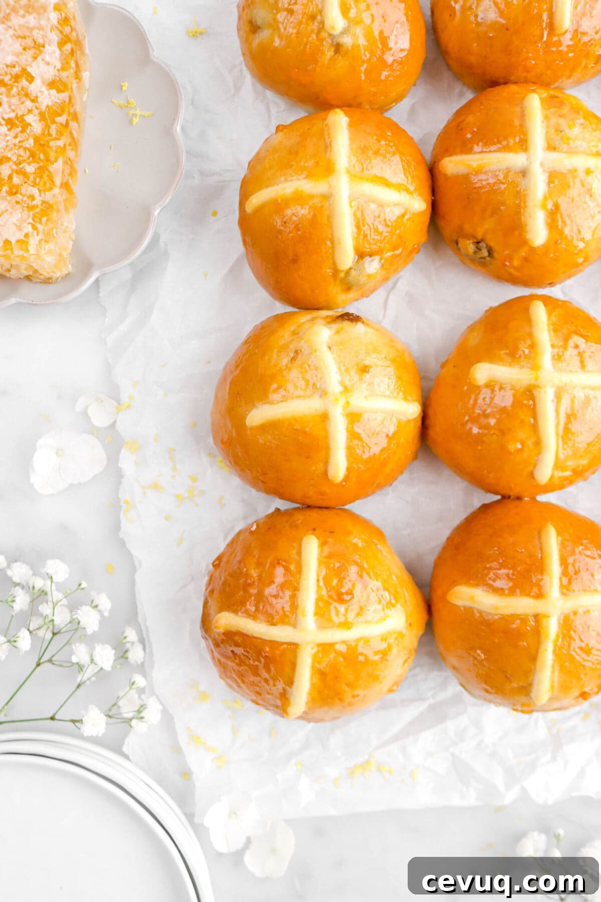 close up overhead of hot cross buns with white flowers and lemon zest