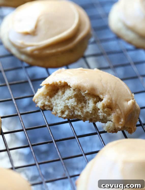 Frosted banana cookies on a wire rack with a bite missing from one cookie.