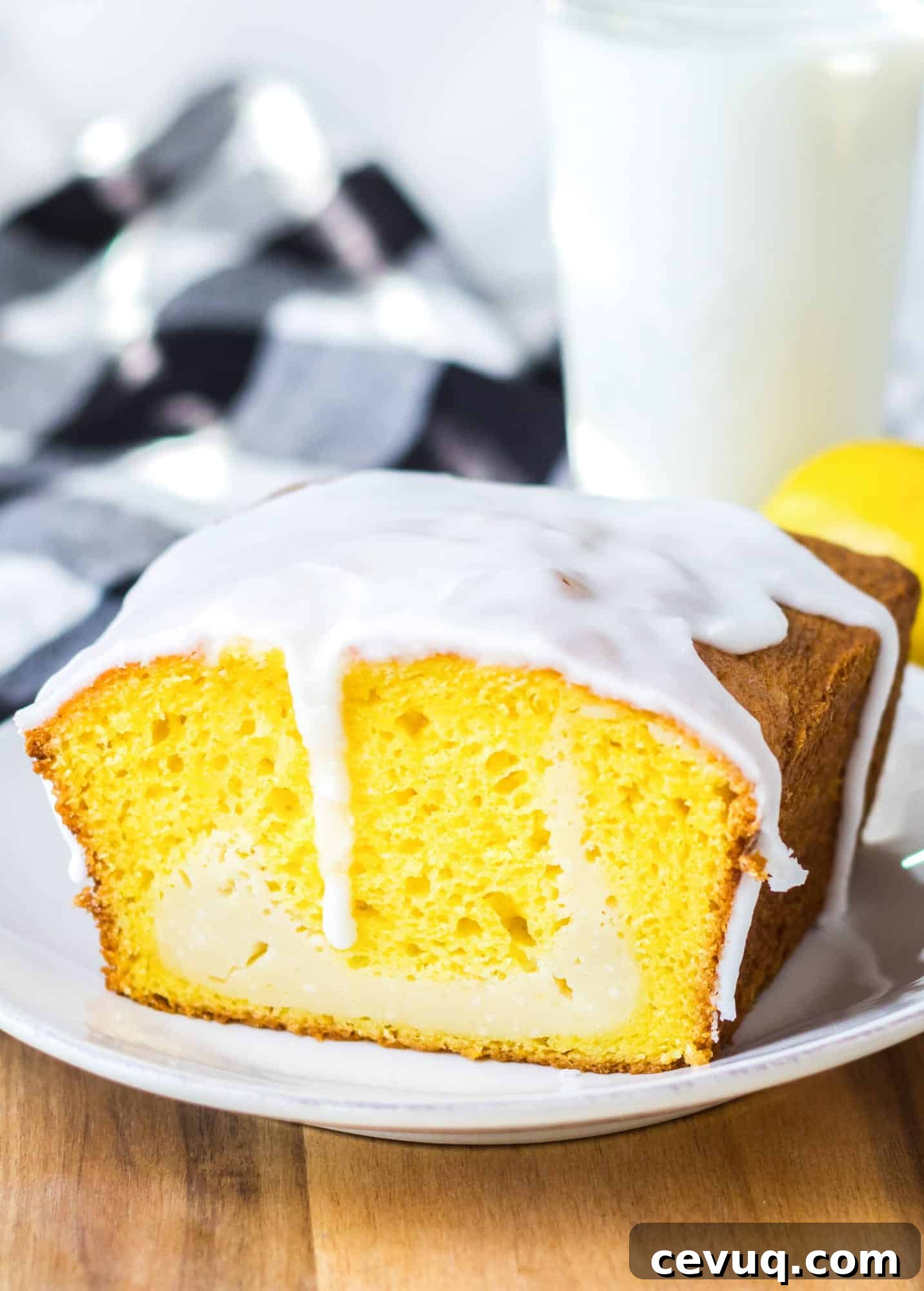 Lemon cheesecake loaf cake with the icing dripping off, placed on a white plate, with a glass of milk in the background.