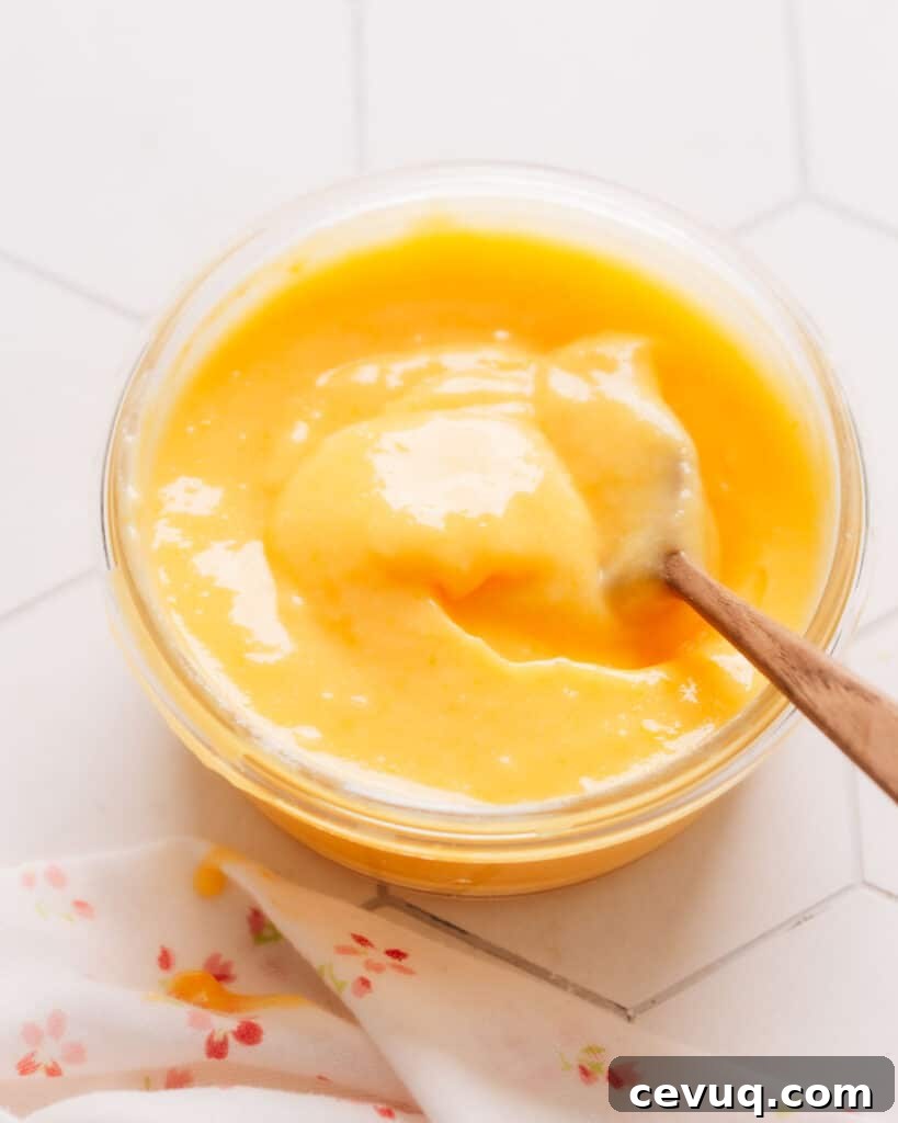 Fresh lemon curd filling in a small cup with a wooden spoon inside