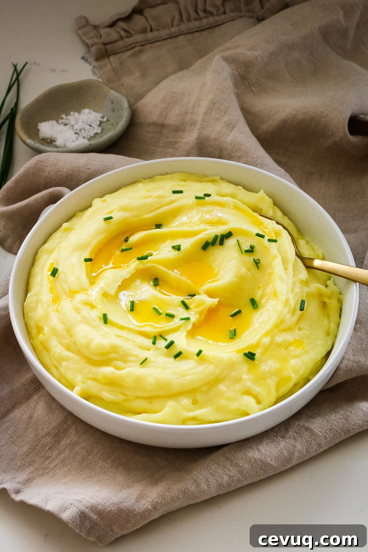 Mashed potatoes in a white bowl with a spoon in it.