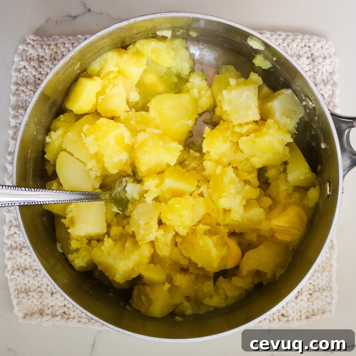 Potatoes in a mixing bowl with a fork in it.