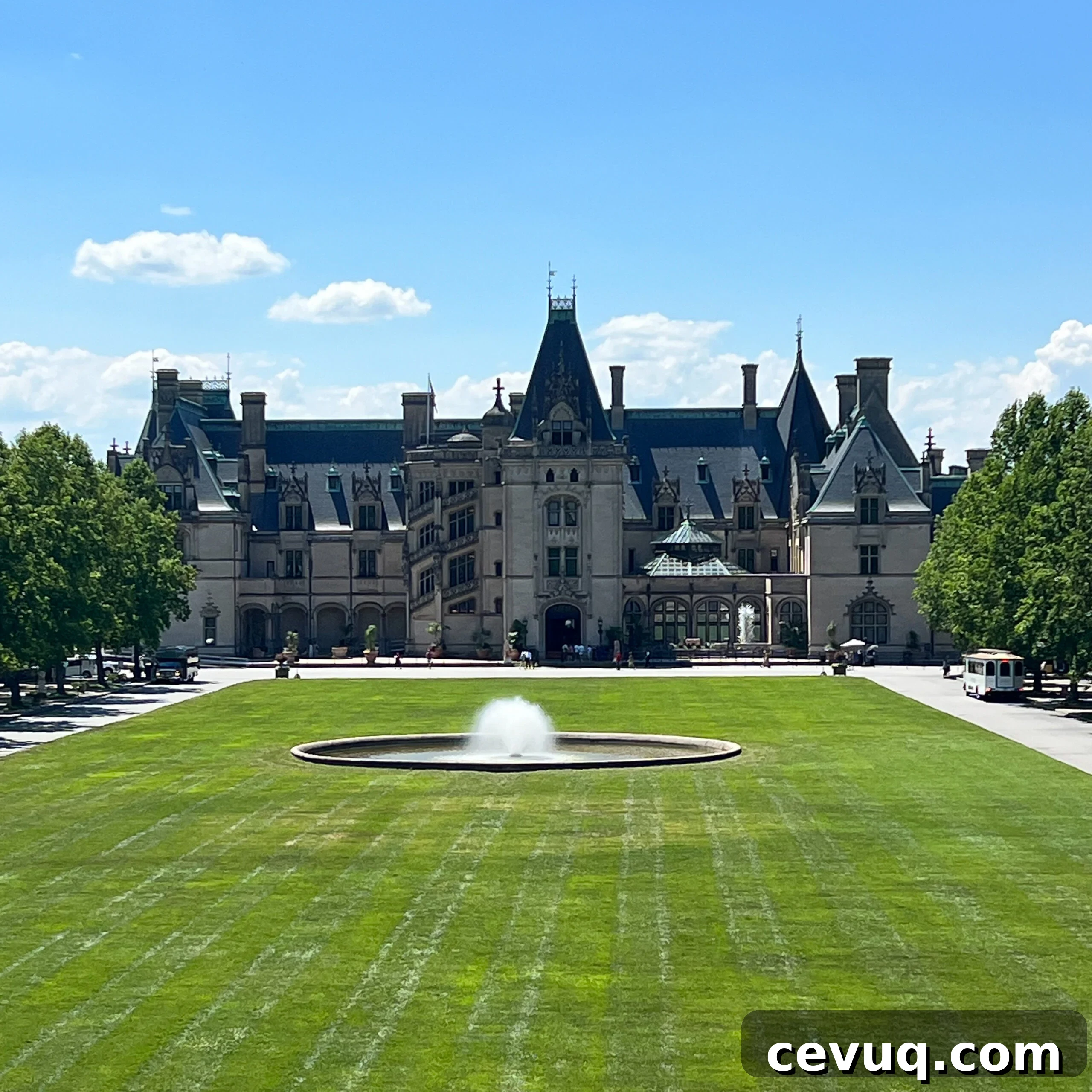 A large historic mansion with a central fountain on a green lawn.