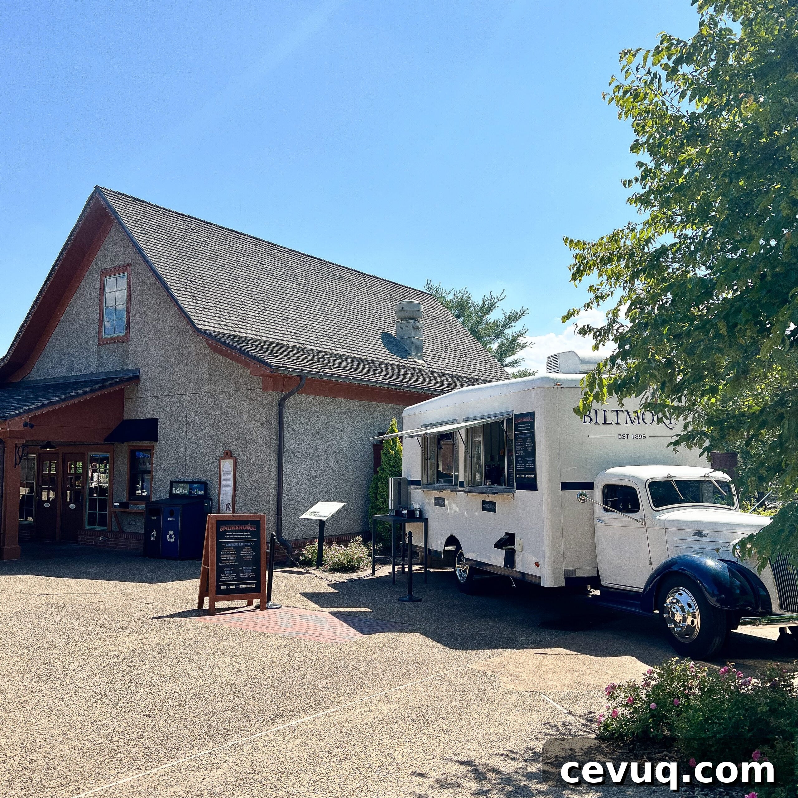 A white food truck parked outside a rustic building on a sunny day.