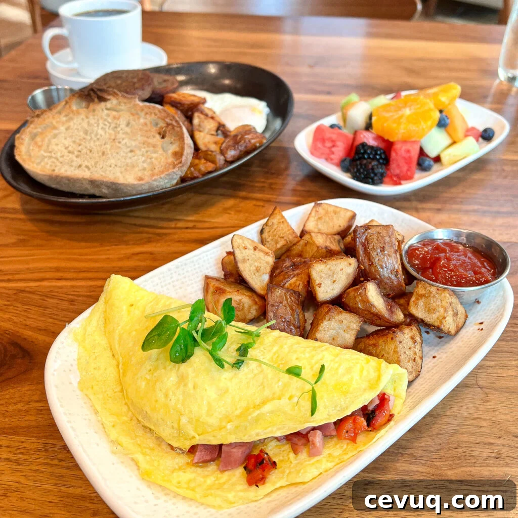 A breakfast spread with omelet, roasted potatoes, fruit, and coffee on a wooden table.