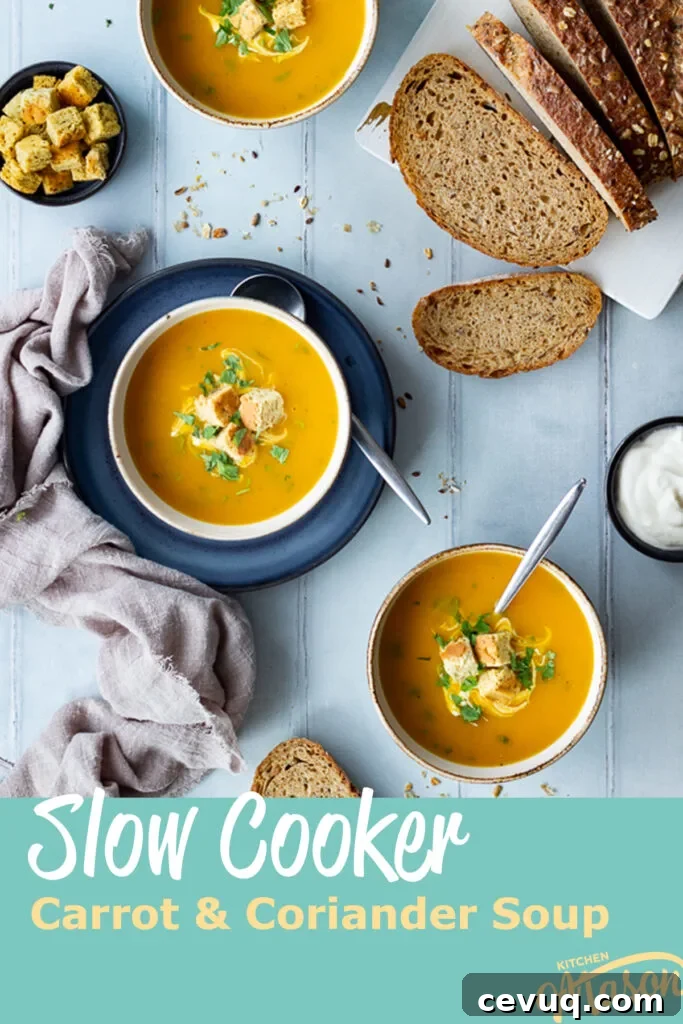 3 bowls of slow cooker carrot and coriander soup, one of which set on a blue plate, all topped with croutons, soured cream and coriander. There's a sliced loaf of bread, pot of soured cream, pot of croutons, spoons and a light brown linen napkin in the background. Set on a cool grey wood effect backdrop. A text overlay says 