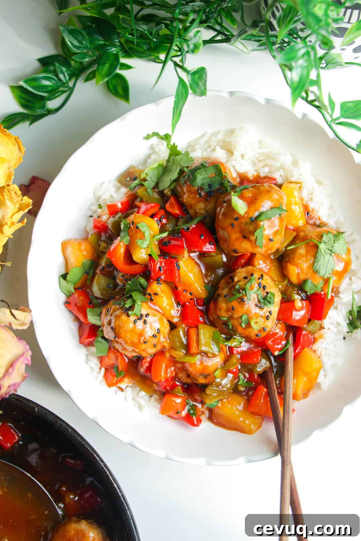 Sweet and sour meatballs over rice in a white bowl.