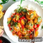 Sweet and sour meatballs over rice in a white bowl.