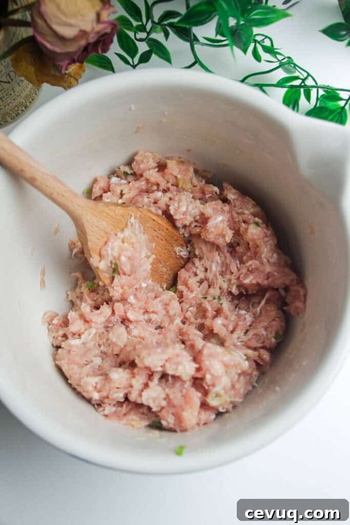 Ground chicken mixed with other meatball ingredients in a bowl.
