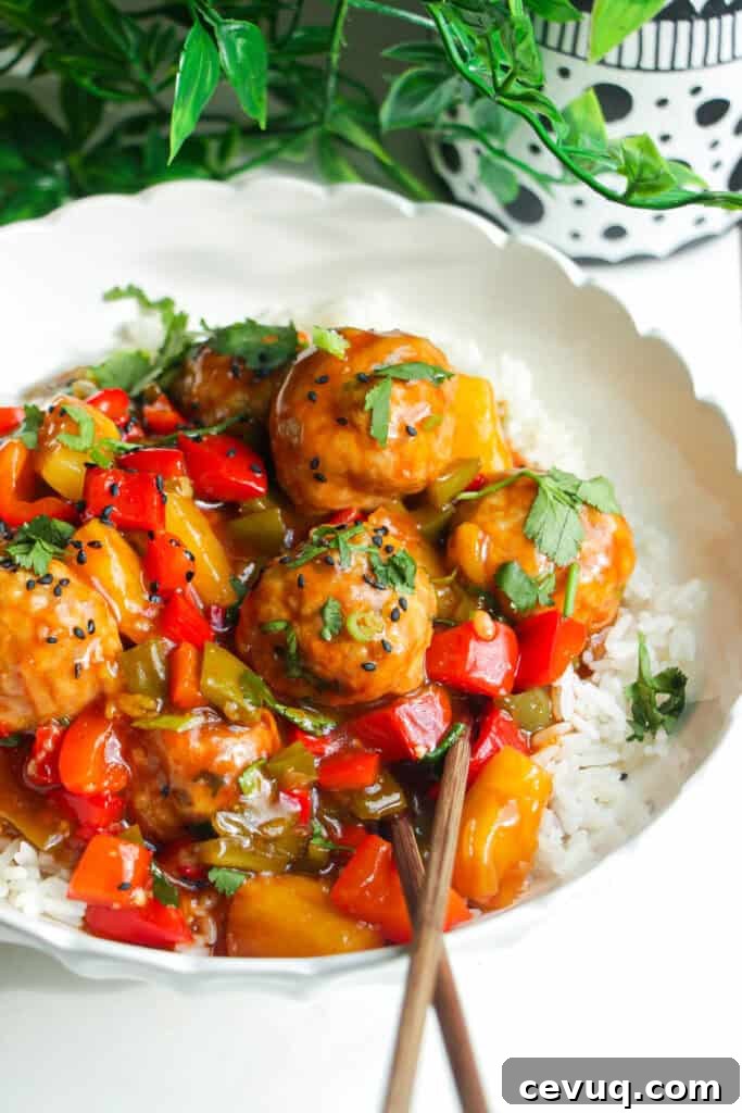 Sweet and sour meatballs over rice in a white bowl.