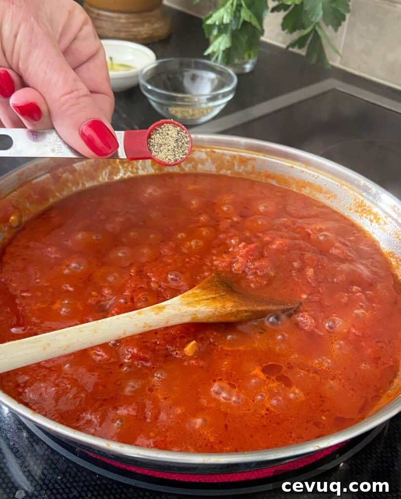 Black pepper being added to tomato sauce in pan.