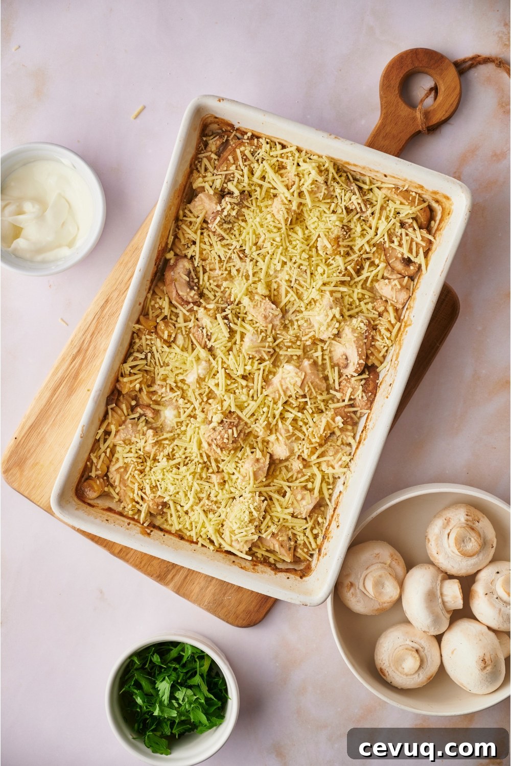 Chicken and mushroom casserole covered in shredded cheese. The casserole is in a white baking dish and on top of a wooden board.